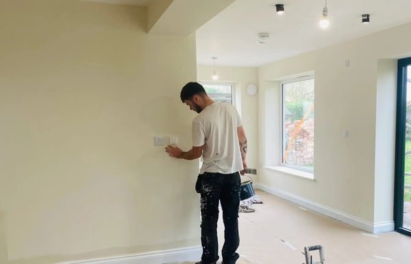 Painter inspecting a wall while holding tools.