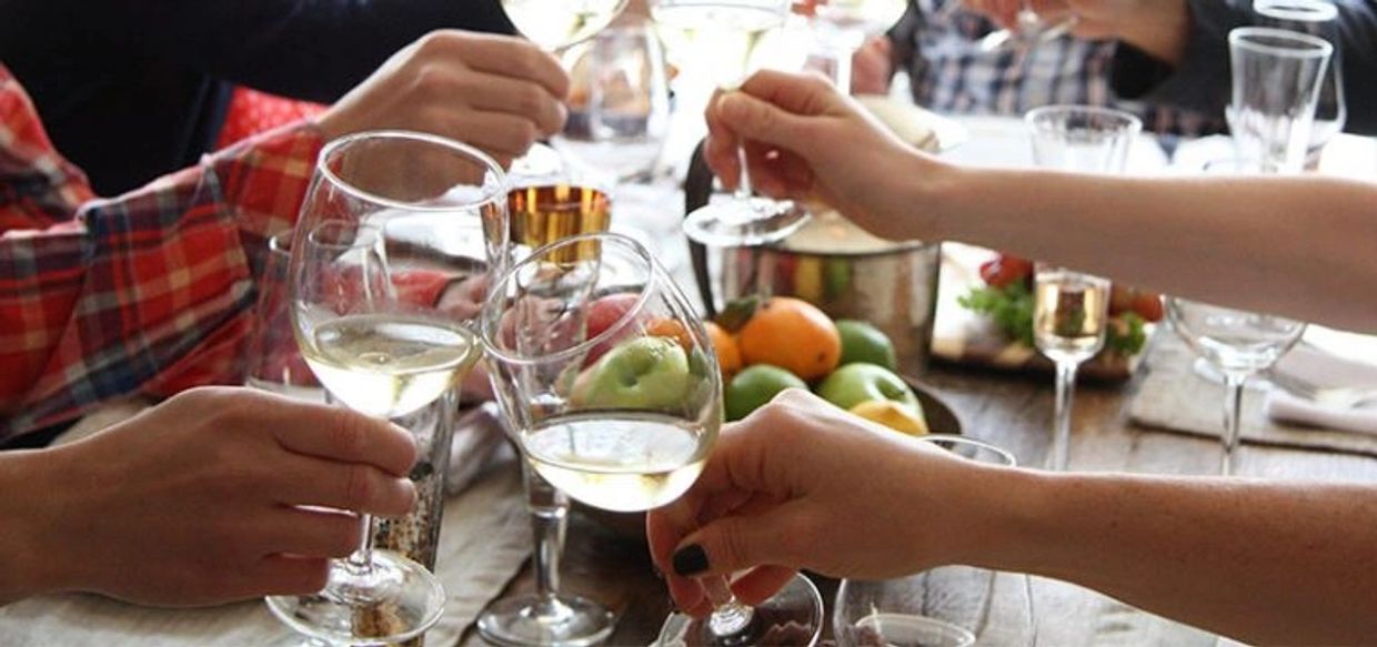 Hands of several people toasting with white wine at a table.