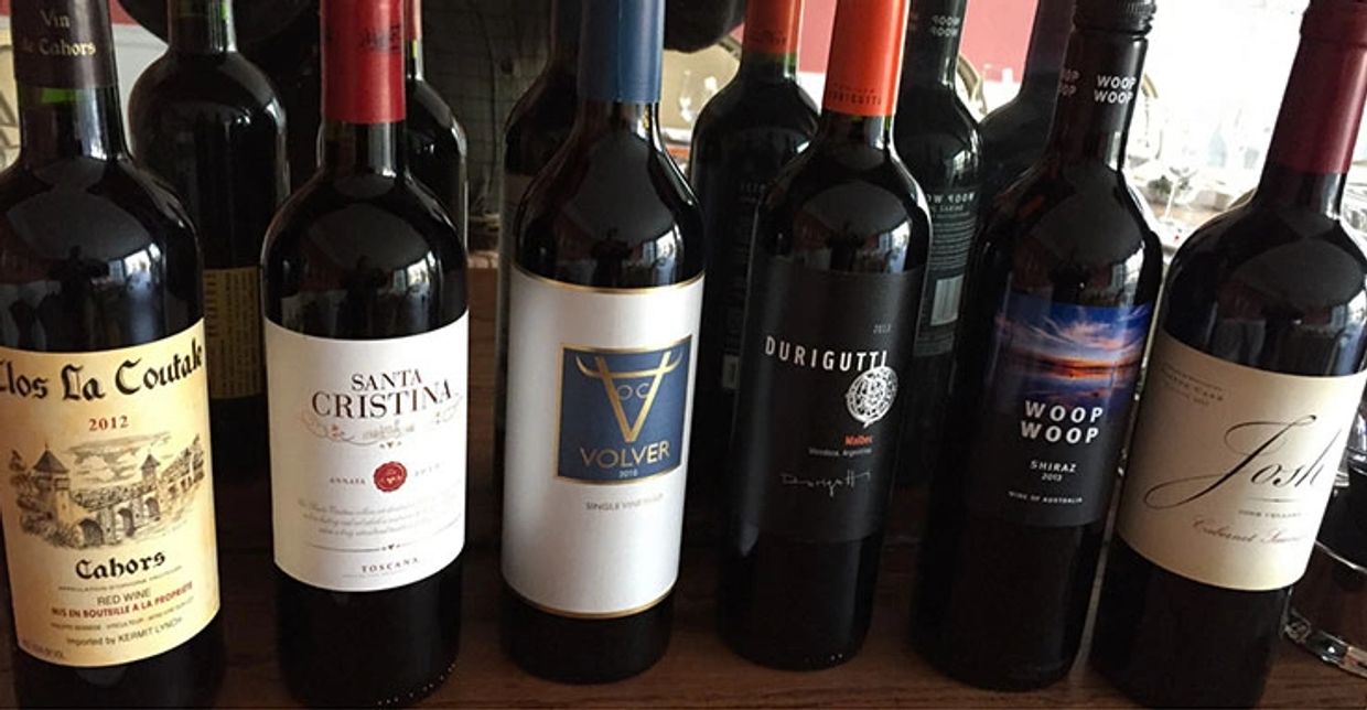 Line of various bottles of red wine on a table.