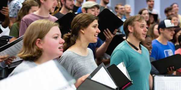 Group of people singing together with music sheets.