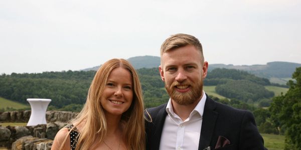 Smiling couple posing outdoors with scenic background.