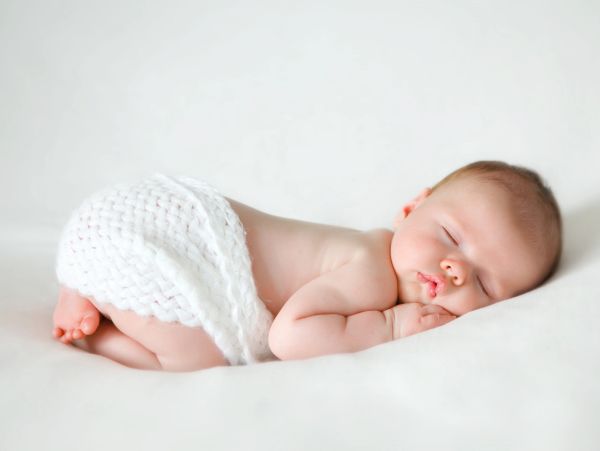 Newborn baby peacefully sleeping on a soft white surface.