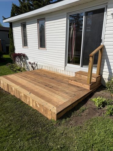 New wooden deck with steps and railing outside a white house.