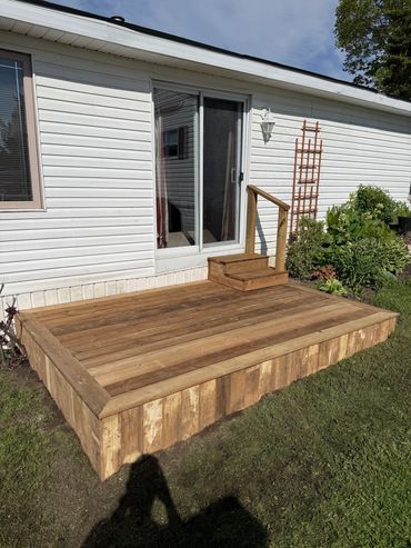 New wooden deck with small steps outside white house.