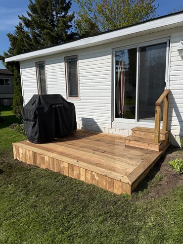 New wooden deck with grill cover outside white house.