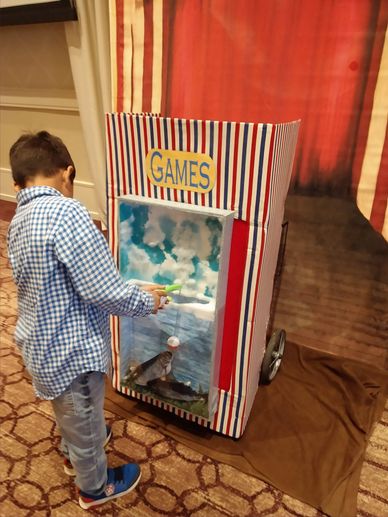 boy in blue shirt plays ice fishing carnival game in a ballroom at the briar club w/ stage backdrop