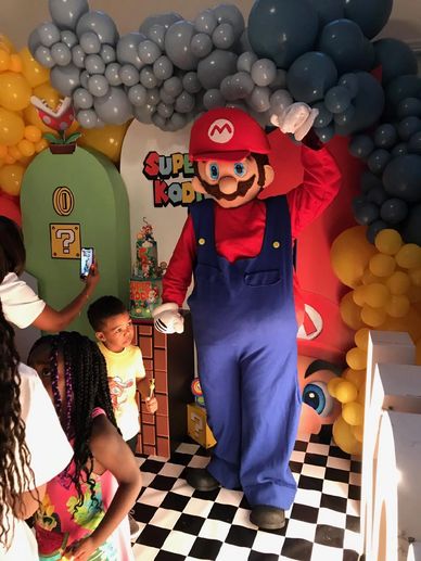 Cosplay Mario mascot video game character at Katy birthday party with kids by the cake & balloons
