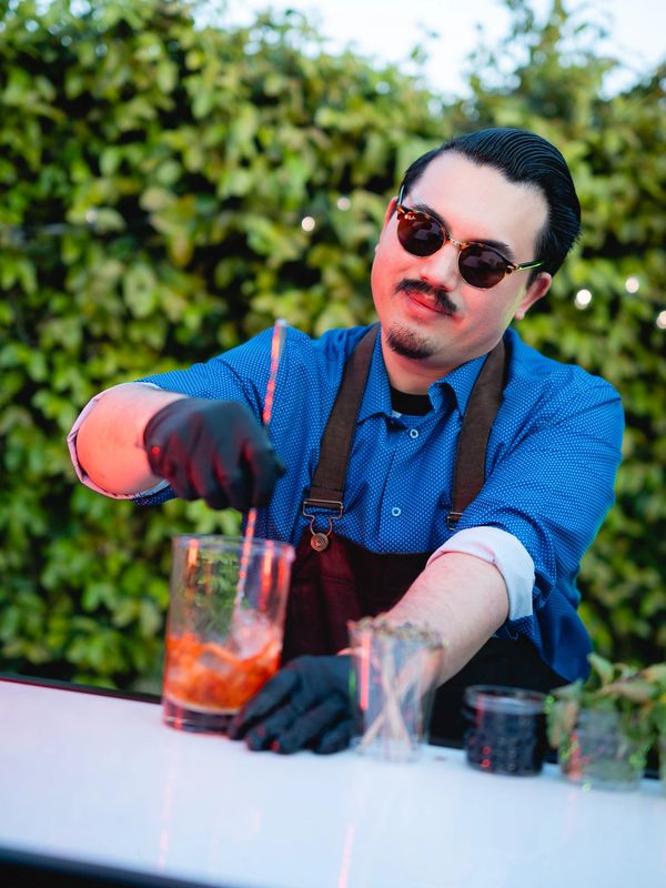 Bartender in sunglasses stirring a cocktail at an outdoor event bar setup in Orange County