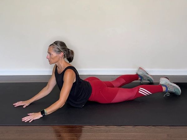 Woman doing a prone stretch exercise on a black mat.