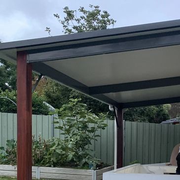Covered outdoor patio with wooden posts and garden beds.