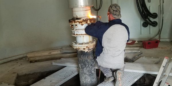 Worker welding a large industrial pipe indoors.