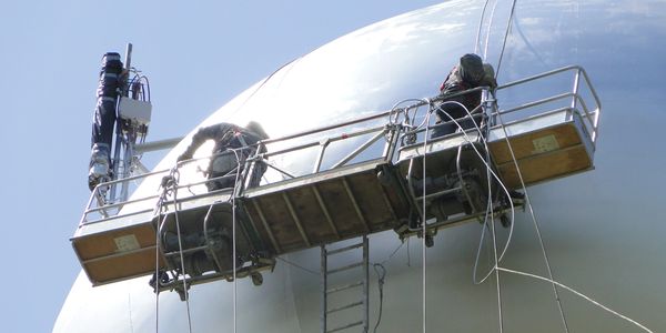 Two workers on a suspended platform inspecting a large spherical structure.