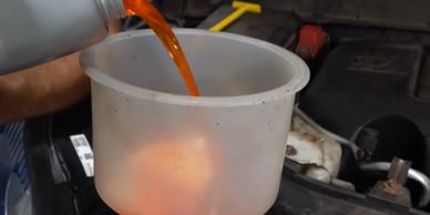Pouring orange liquid into a translucent container in a vehicle engine bay.
