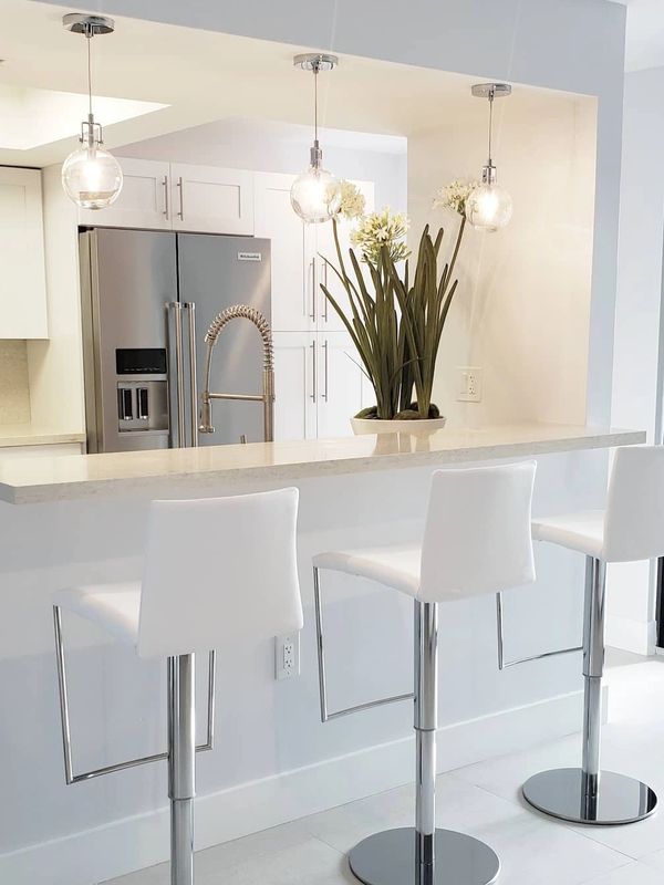 Modern white kitchen with sleek bar stools and pendant lights.