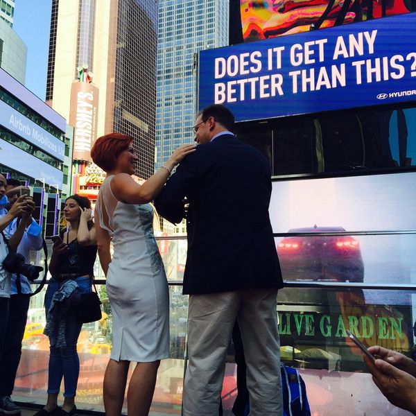 A bride and groom are celebrating their ceremony in Times Square with a billboard that says "Does it