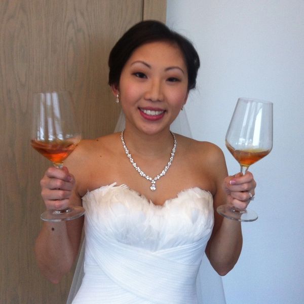 A smiling bride is toasting the future with a wine glass in both  hands.