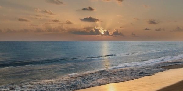 Sunset over a calm ocean with waves gently hitting the sandy shore.