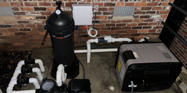 Outdoor pool filtration and pump system setup against brick wall.