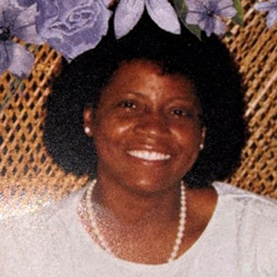 Smiling woman with pearl necklace and floral background.
