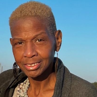 Smiling woman with short blonde hair and large earrings outdoors.