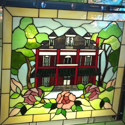 Stained glass window depicting a red house with surrounding trees and flowers.