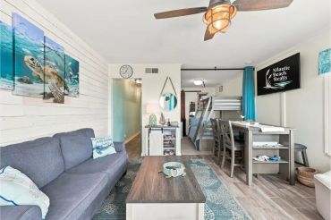 Cozy beach-themed living room with gray sofa and dining area.