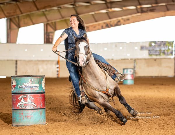 Woman barrel racing on a horse inside an arena.