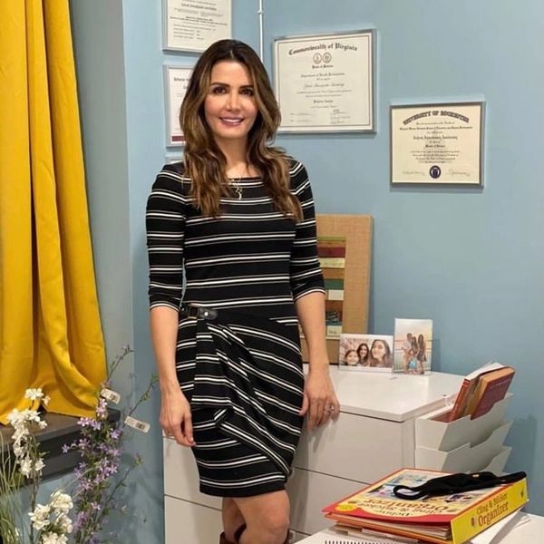 Woman in a striped dress standing by a desk with certificates on the wall.