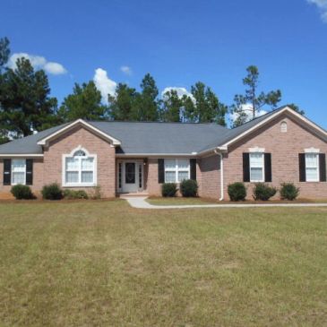 Single-story brick house with a large yard and blue sky.