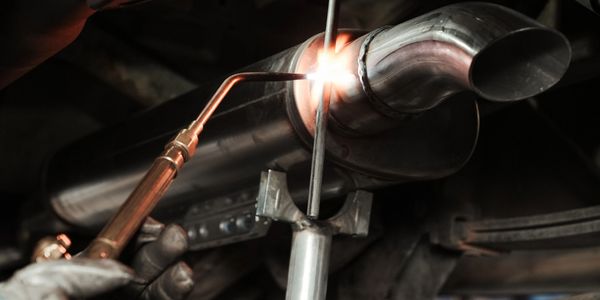 Welding a metal exhaust pipe on a vehicle.