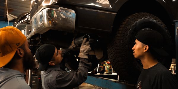 Three men inspecting a car exhaust in a garage.