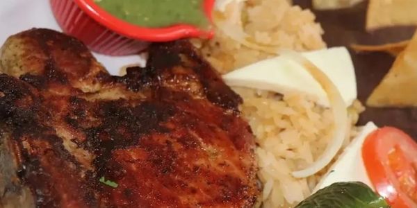 Grilled meat served with rice, beans, and green salsa.