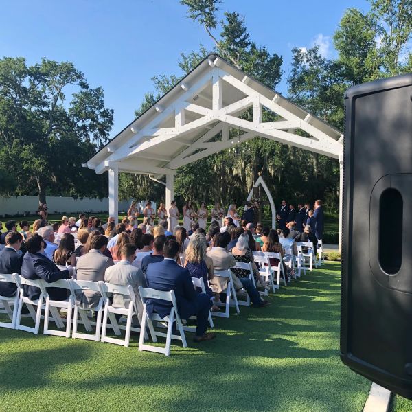 Outdoor wedding ceremony with guests seated under a white pavilion.