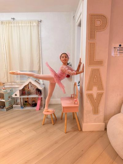 A young ballerina practices ballet in a pink tutu at home.