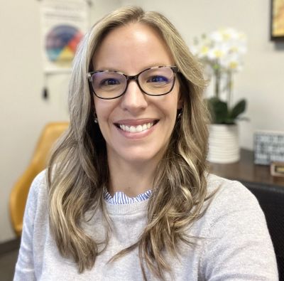 Smiling woman with glasses in an office setting.