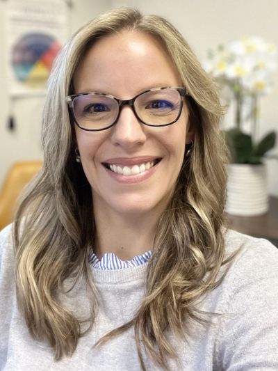 Smiling woman with glasses and long hair indoors.