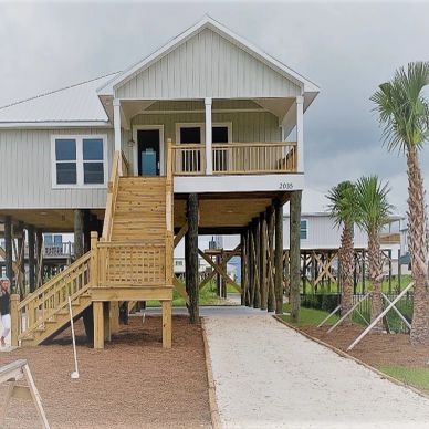 Elevated house on stilts with a wooden staircase and palm trees.