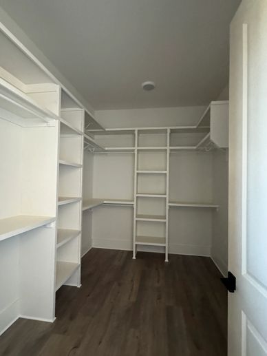 Empty walk-in closet with white shelves and wooden floor.