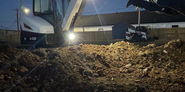 Bobcat excavator digging soil at night with bright lights.
