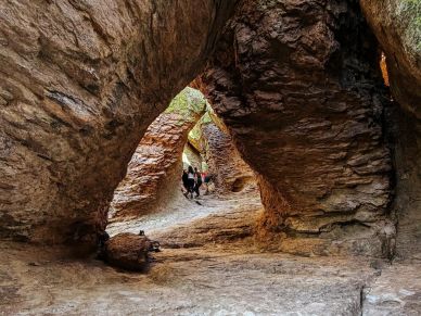 People exploring a natural rock formation cave with light filtering in.