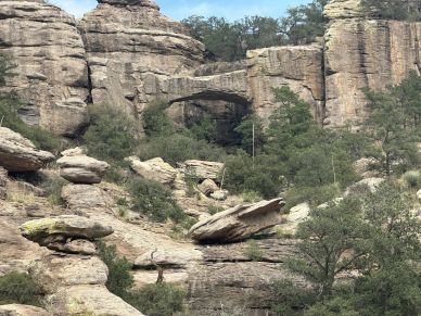 Natural rock formations and a stone bridge in a rugged landscape with greenery.