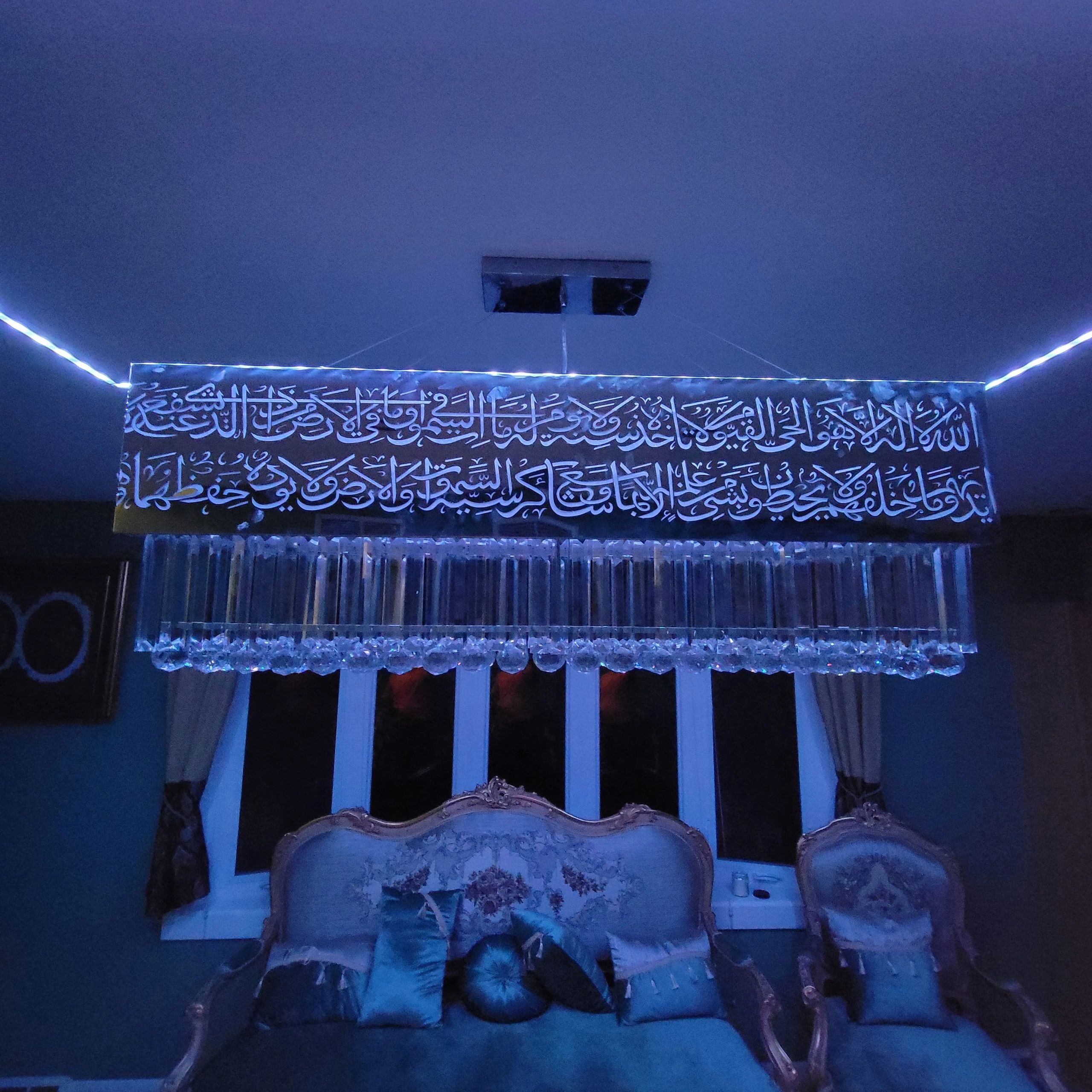 Elegant chandelier with Arabic calligraphy hangs above a classic sofa set in a dimly lit room.