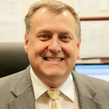 Smiling man in a suit and tie sitting in an office.