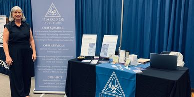 Woman standing beside a Diakonos Solutions informational booth with brochures and display items.