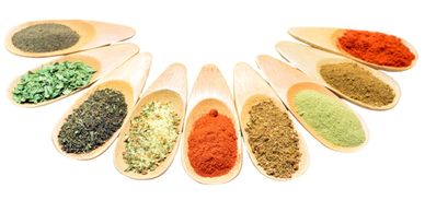 Wooden spoons filled with various colorful spices arranged in a semicircle.