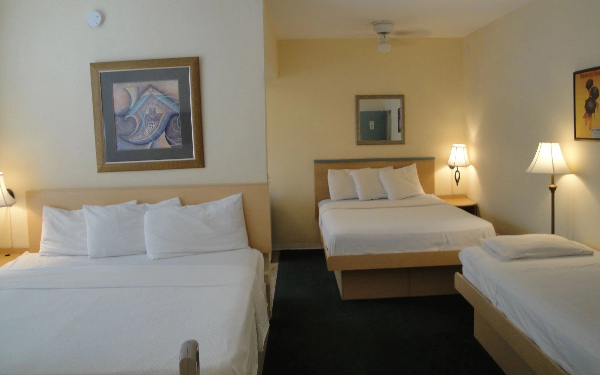 A hotel room with three beds, lamps, and artwork on the walls.