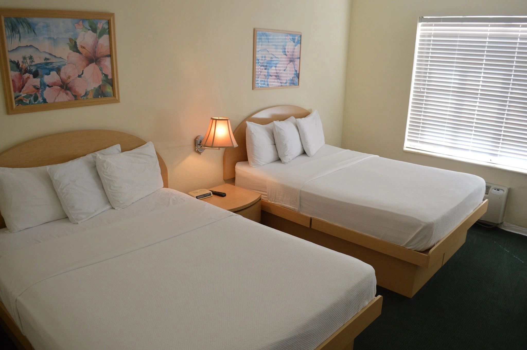 A hotel room with two twin beds, cream walls, and green carpet.