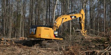 Yellow CAT excavator clearing a forest area with fallen trees.