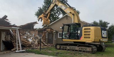 A CAT excavator demolishes a house in a residential area.