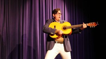 Man energetically playing guitar on stage.